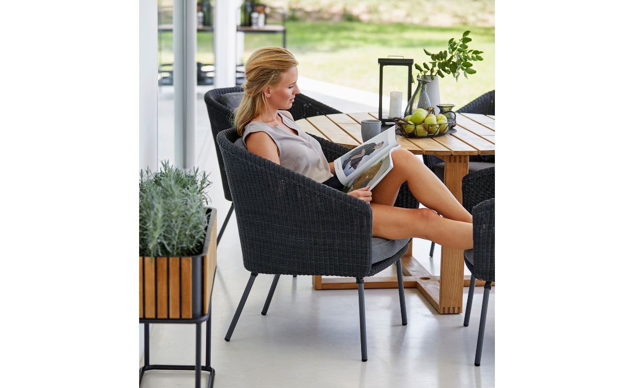 Cane-line Mega Outdoor Dining Chair in Dark Grey with Light Grey Cushions with a lady reading - Danish Design Co Singapore