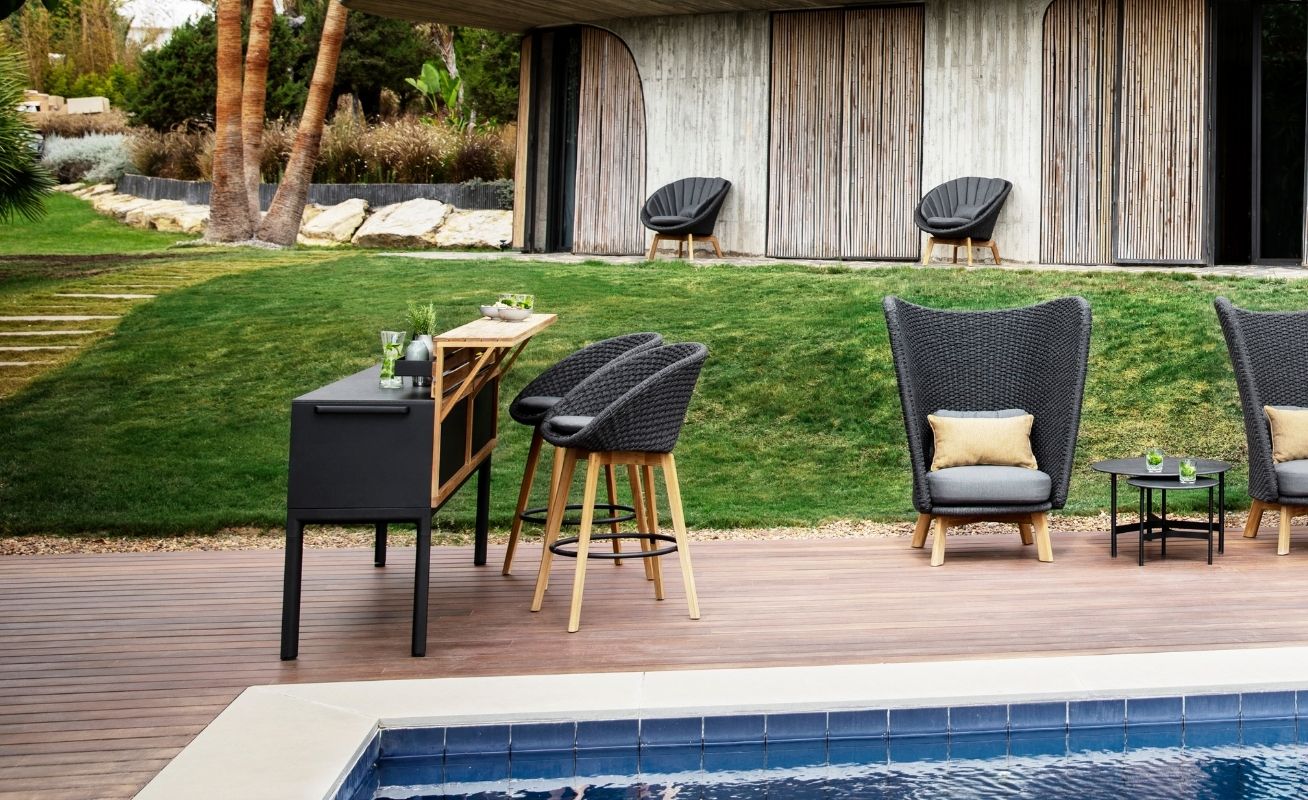 Cane-line Peacock Outdoor Bar Chair in dark grey with a light cushion by pool - Danish Design Co Singapore