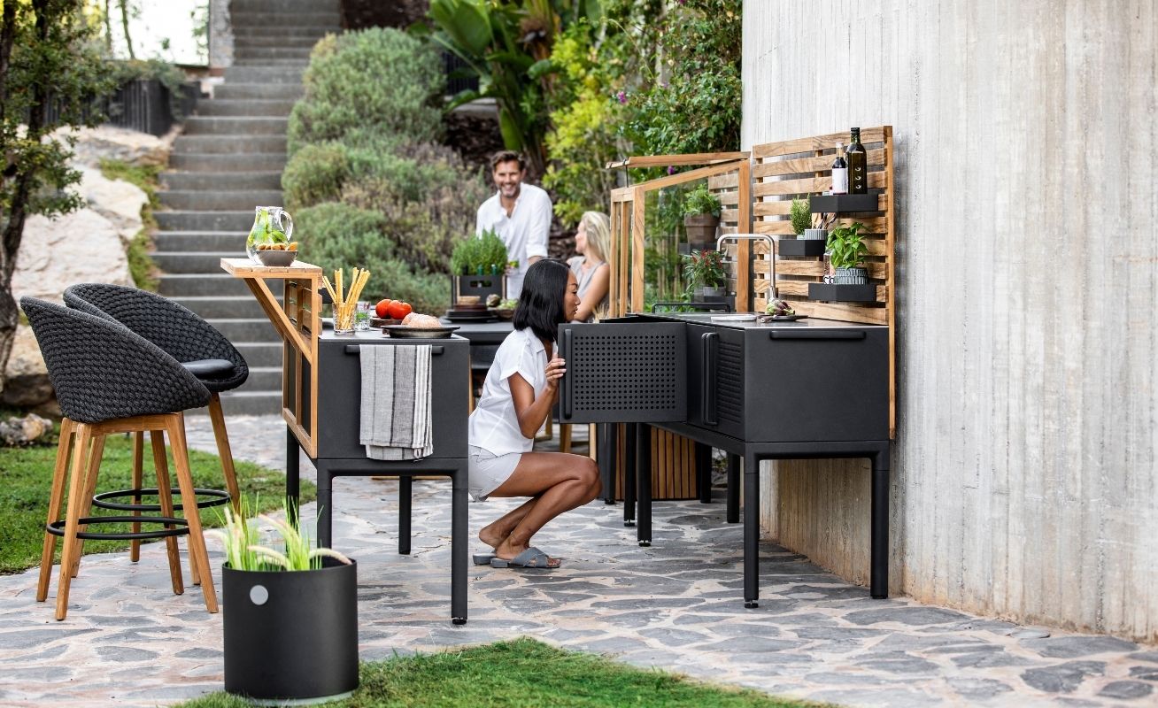 Cane-line Peacock Outdoor Bar Chair in dark grey with a light cushion in outside setting - Danish Design Co Singapore